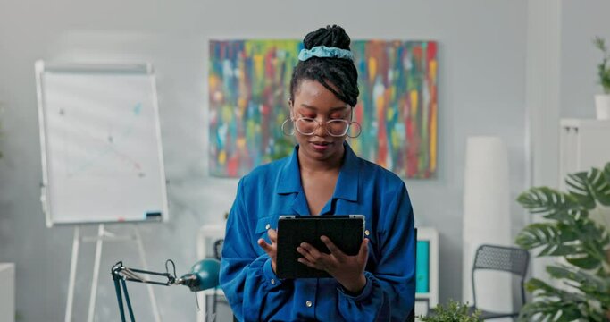 Corporate job corporate duties elegant beautiful ambitious businesswoman stands in office with tablet in hands does report writes back messages empties email inbox, smiles at camera
