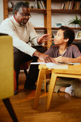 Fototapeta na wymiar An African-American grandfather is sitting at home with his grandson and helping him with homework.