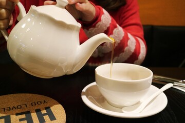 A woman picks up a white teapot and is pouring tea into a white cup