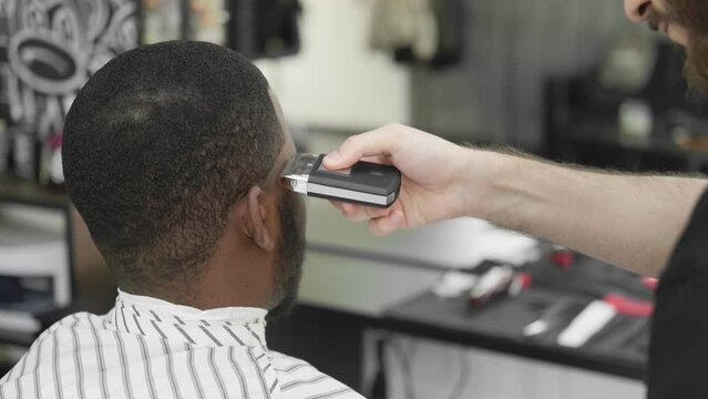 A young African visits a hairdresser. Tidying up the beard with the help of a hairdresser. Personal care, male beauty, beard trim
