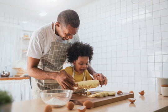 Happy Smiling African American Father and son Cooking and kneading dough, Black African male and his boy playing while preparing food in kitchen