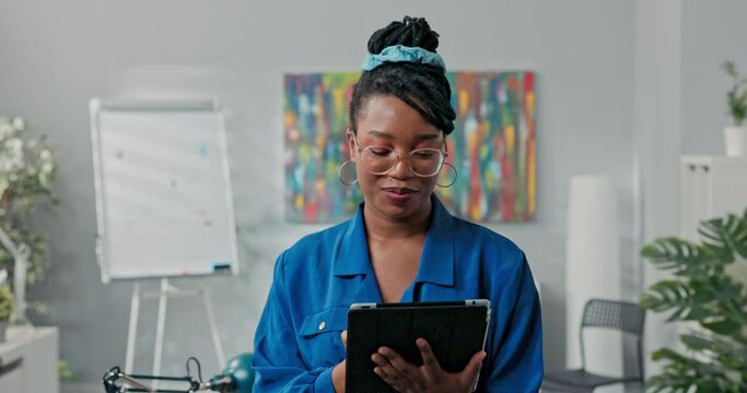 Corporate job corporate duties elegant beautiful ambitious businesswoman stands in office with tablet in hands does report writes back messages empties email inbox, smiles at camera
