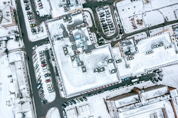 rooftop of apartment building with ventilation systems and courtyard with parked cars covered by snow. drone photo.