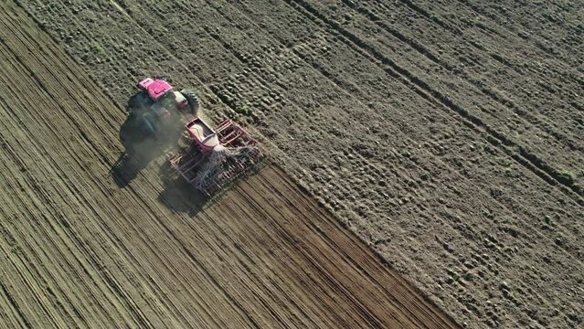 Modern unmanned tractor with a seeding unit operating on arable land during the season. Agricultural machine controlled remotely by a farmer from the ground. Concept of agribusiness. Aerial view.