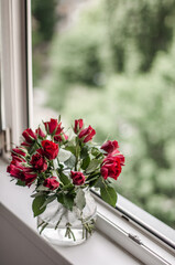 A bouquet of red roses in the glass vase with water on the windowsill