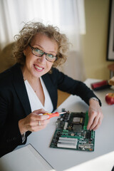 Middle-aged woman looking at camera and repair the computer component.