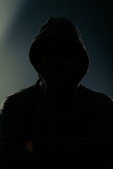 Mystery man with hidden face in a hood in the dark.