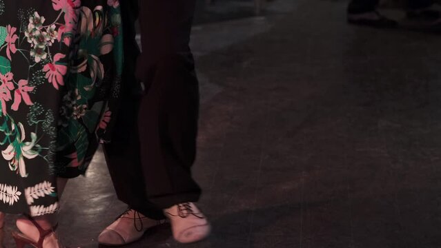 Unrecognizable dance partners enjoy the movement on dark background. Milonga in vintage cafe. Slow motion.