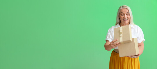 Smiling mature woman opening gift box on green background with space for text. International...