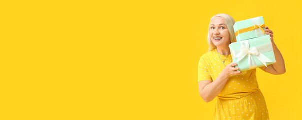Smiling mature woman with gifts on yellow background with space for text. International Women's Day celebration
