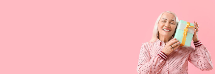 Happy mature woman with gift on pink background with space for text. International Women's Day celebration