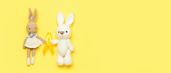 Bunny toys with golden awareness ribbon on yellow background with space for text. International Childhood Cancer Day