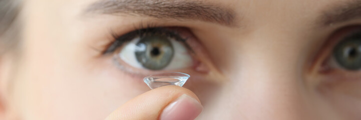 Soft contact lens on female finger against background of female eyes