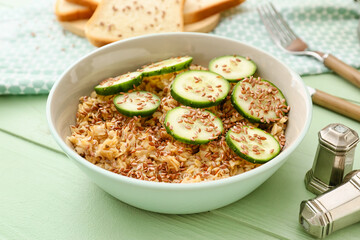 Bowl with tasty oatmeal, flax seeds and cucumber on table