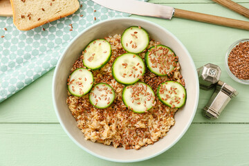 Bowl with tasty oatmeal, flax seeds and cucumber on table