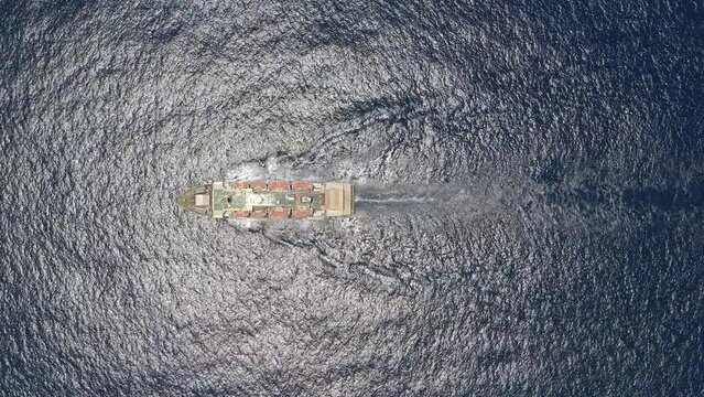 Aerial drone video of container ship with colourful truck size containers cruising in open ocean. A container ship carries cargo across the ocean. Transportation. Delivery. Logistics. Aerial 4K shot.