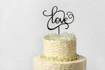 Beautiful wedding cake and topper with word LOVE on light background