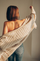 sexy young woman with bare shoulders in knitted cardigan, jeans moves freely in sunlight in white bright room. women's dances and movements. vertically, selective focus