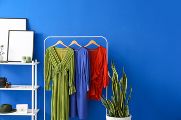 Hanger with stylish dresses, shelf unit with female accessories and blank photo frames near color...