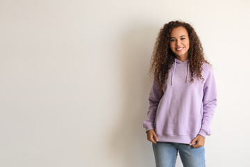 Beautiful young African-American woman in stylish hoodie on light background