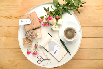 Tray with cup of coffee, gift boxes, notebook and roses on wooden background