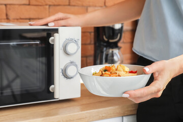 Woman holding bowl with delicious food near counter with microwave oven