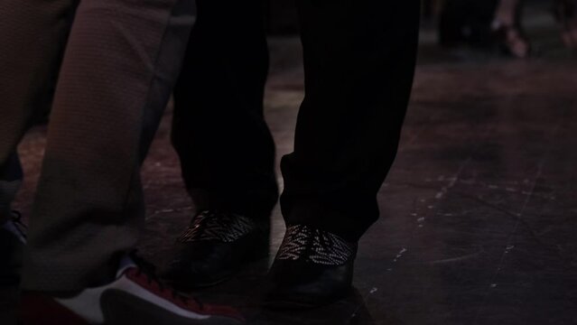 Close-up of legs dancing tango in slow motion on dark floor. Milonga in vintage cafe.