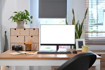 Front view computer with white blank screen, houseplant and supplies on wooden desk.