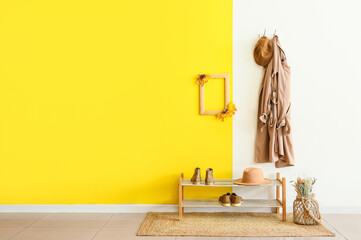 Stylish jacket and hat with frame hanging on color wall in hallway
