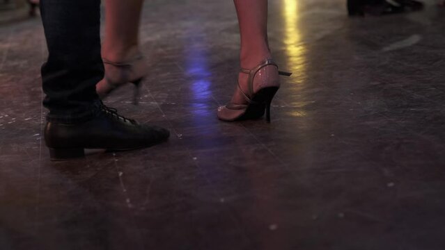Dancing legs of unknown couple performing argentinian tango on wooden floor in dark vintage cafe, close-up. Man and woman enjoying playful figures on milonga.