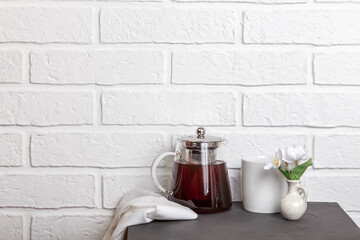 Kitchen background, white brick wall in loft style. Teapot and cup on the table. Morning tea