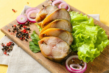 Wooden board with pieces of smoked mackerel fish on yellow background, closeup