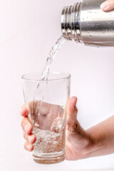 The hand was holding the stainless water bottle to pour water into the glass.