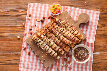Board of tasty thin pancakes with chocolate paste and nuts on wooden background