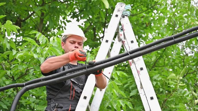 The electrician fastens corrugated pipes with wire using ties. Worker connecting cables for photovoltaic solar panel system.