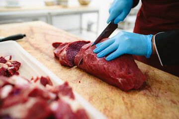 Butcher cutting slices of raw meat on wooden board