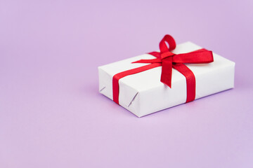 Valentine's Day or birthday concept with copy space. White gift box with red ribbon on purple papper