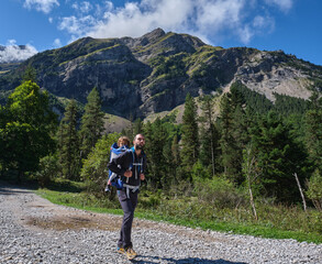 father with little daughter in baby carrier backpack hiking in mountains. family adventure, outdoor vacation.