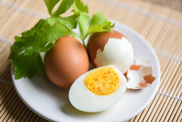Eggs breakfast, fresh peeled eggs menu food boiled eggs and eggshell on white plate decorated with leaves green celery on wooden background, egg cooking healthy eating concept