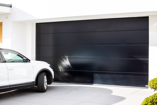 Modernes schwarzes Garagentor mit davor parkendem PKW