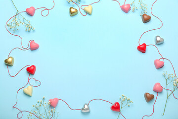 Frame made of tasty heart-shaped candies and flowers for Valentine's Day celebration on blue background