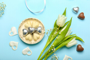 Composition with tasty heart-shaped candies and flowers for Valentine's Day celebration on blue background