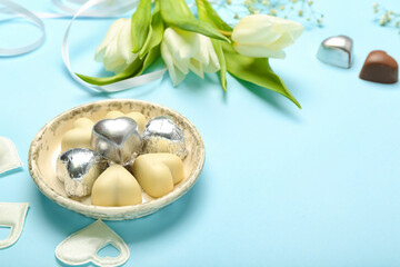 Composition with tasty heart-shaped candies and flowers for Valentine's Day celebration on blue background