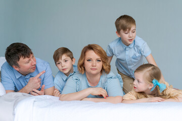Happy caucasian big family lie in bedroom on bed and smile. Dressed in blue clothes are having fun together. Parents and children two sons and a cute daughter