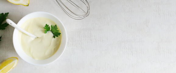 Homemade mayonnaise in a white bowl with parsley leaf and lemons in the background. The concept of proper nutrition. Top view. copy space. Horizontal orientation. Banner.