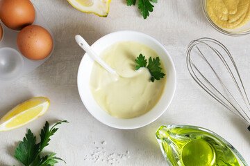 Homemade mayonnaise in a white bowl with parsley leaf and ingredients around. The concept of proper...