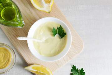 Homemade mayonnaise in a white bowl with parsley leaf and olive oil. The concept of prepared homemade food. Horizontal orientation. Top view. Copy space.