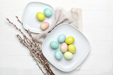 Plates with painted Easter eggs, willow branches and napkin on white wooden background