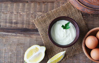 Homemade mayonnaise in a brown bowl with ingredients around on a wooden table. The concept of...