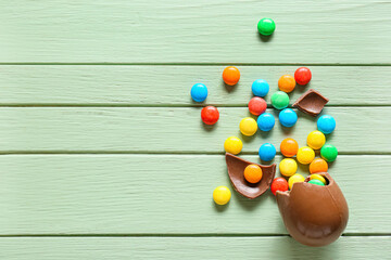 Broken chocolate Easter egg with candies on green wooden background